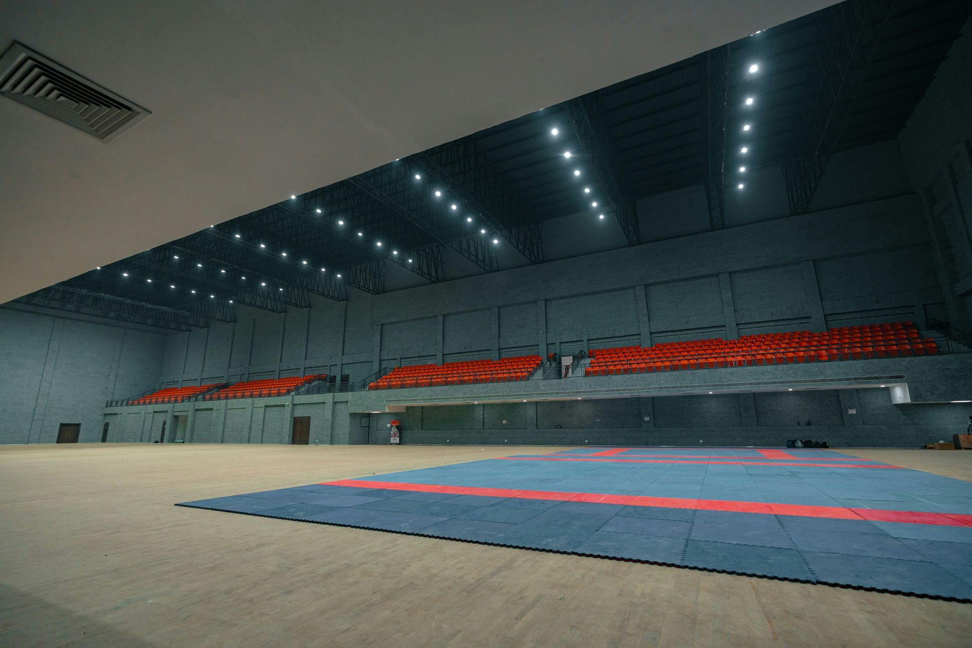 Empty indoor sports arena with red seating and blue mats.